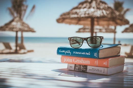 photo of sunglasses on top of some books under a beach cabana with the waves in the background