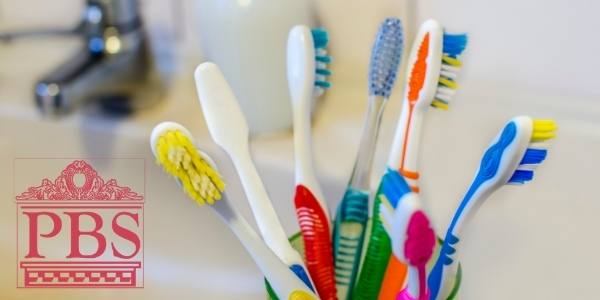 Photo of toothbrushes in a glass cup on a sink.
